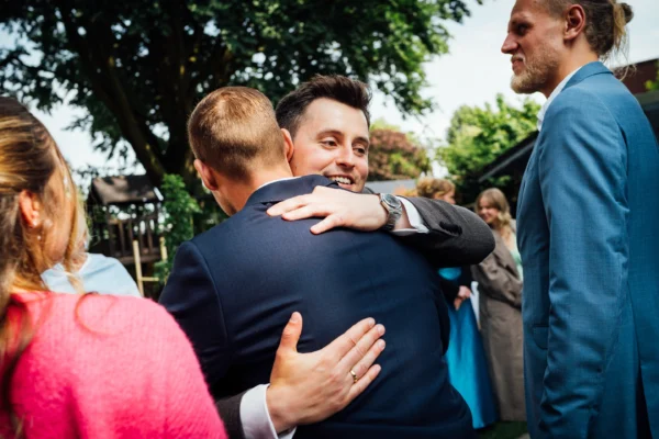 Der Bräutigam umarmt während des Sektempfangs einen Gast