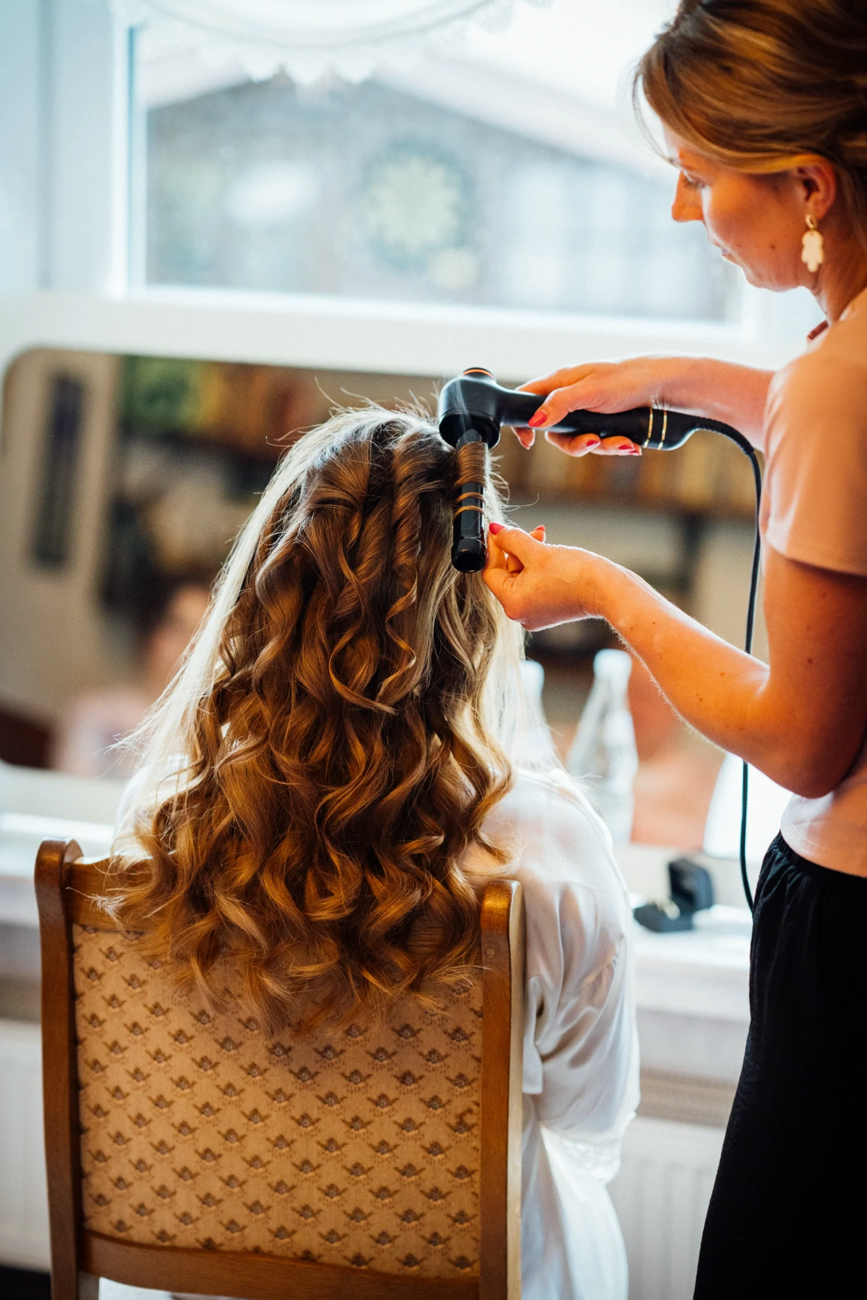 Eine Stylistin dreht Locken in die Haare der Braut